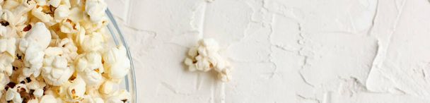 sztandar popcornu w przezroczystej szklanej misce na białym stole z kilkoma popcornami obok miski. Widok góry. Przestrzeń chroniona - Zdjęcie, obraz