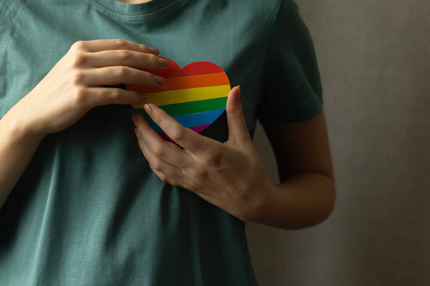 Девочка-подросток, держащая сердце в радужных цветах ЛГБТ. Гордость месяц, гей и лесбиянка толерантность скрытые фоновое фото - Фото, изображение