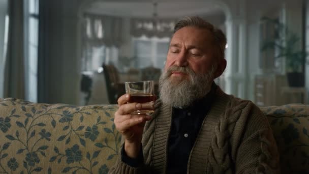 Старый бизнесмен сидит на диване с бокалом виски. Портрет старшего джентльмена - Кадры, видео