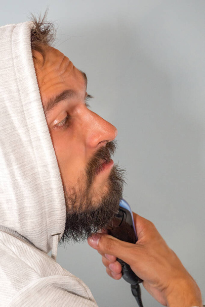 A bearded man shaves with an electric hair clipper - Zdjęcie, obraz