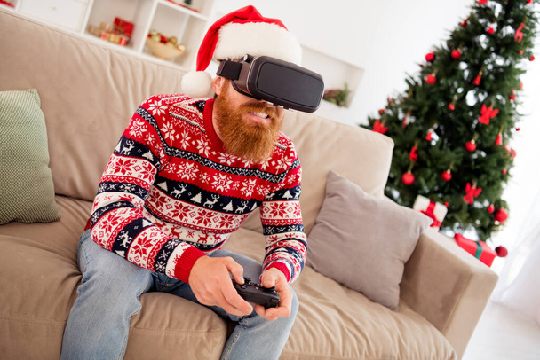 Photo portrait bearded man wearing 3d glasses watching virtual reality playing with joystick on couch - 写真・画像