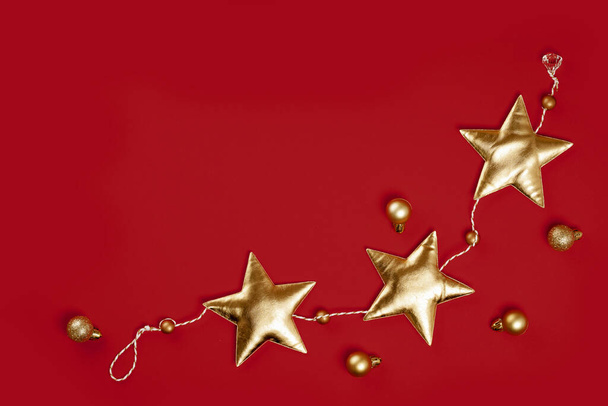 Vrolijk Kerstfeest en Gelukkig Nieuwjaar rijke gouden feestelijke ornamenten. sterren bloemenslinger op rode achtergrond. Partij decoratie grens kopiëren ruimte. Bovenaanzicht - Foto, afbeelding