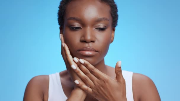 歯痛だ。若いアフリカ系アメリカ人の女性は、歯の痛みに苦しみ、頬に触れ、青い背景 - 映像、動画