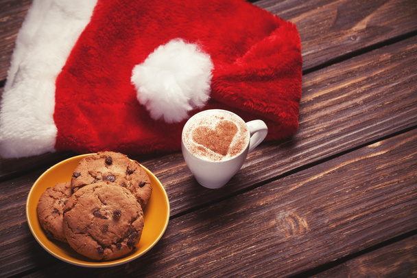 cookie en kopje koffie met KERSTMUTS op houten tafel. - Foto, afbeelding