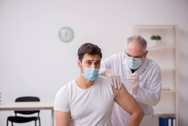 Paciente masculino joven que visita a un médico de edad avanzada en contacto con la vacunación - Foto, Imagen