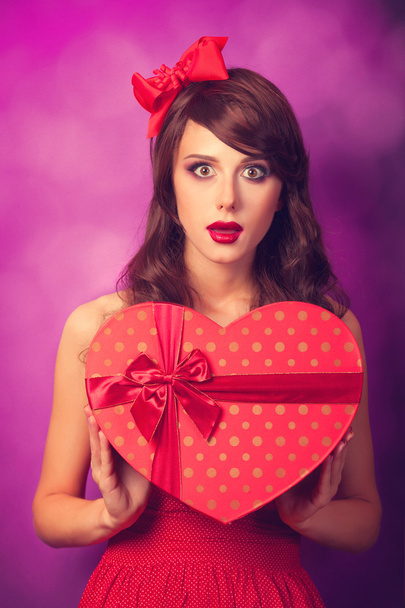 Beautiful brunette girl with heart shape gift on violet backgrou - Zdjęcie, obraz