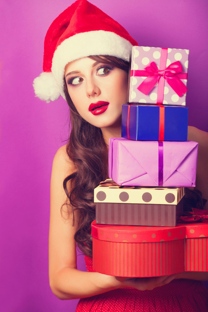 mooie brunette meisje in kerstmuts met giften op violet b - Foto, afbeelding