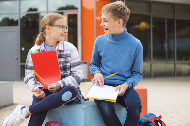 Happy teenagers schoolboy and schoolgirl sitting on schoolyard and joyful talking during break - Foto, Imagen