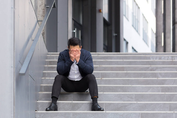 Asian businessman has a severe headache sitting on the stairs near the office - Fotoğraf, Görsel