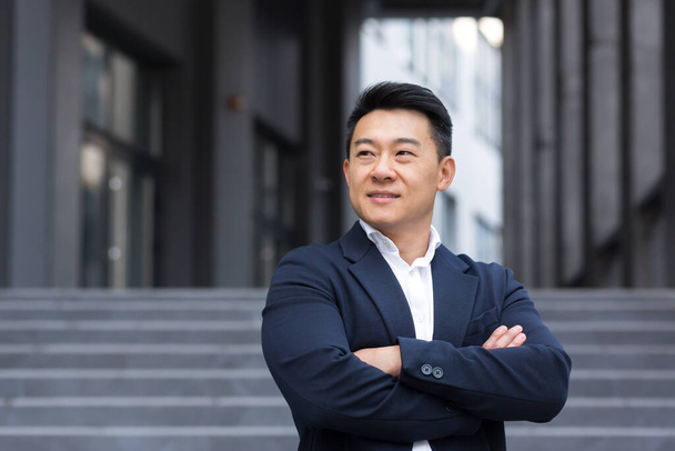Portret van Aziatische vrolijke en succesvolle zakenman in de buurt van kantoor in business suit zelfverzekerde manager verkoper makelaar glimlachend - Foto, afbeelding
