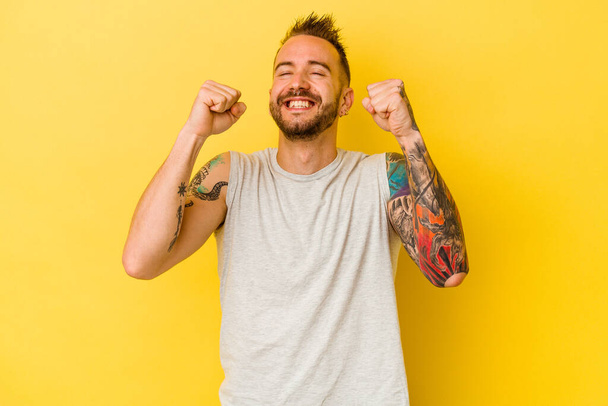 Jeune homme caucasien tatoué isolé sur fond jaune célébrant une victoire, passion et enthousiasme, expression heureuse. - Photo, image