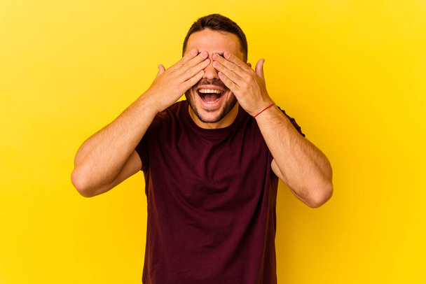 Junger kaukasischer Mann isoliert auf gelbem Hintergrund bedeckt Augen mit Händen, lächelt breit und wartet auf eine Überraschung. - Foto, Bild