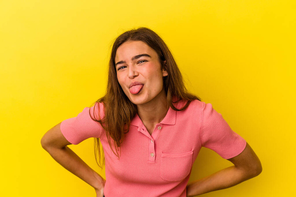 Mujer joven caucásica aislada sobre fondo amarillo divertida y amigable sobresaliendo de la lengua. - Foto, imagen