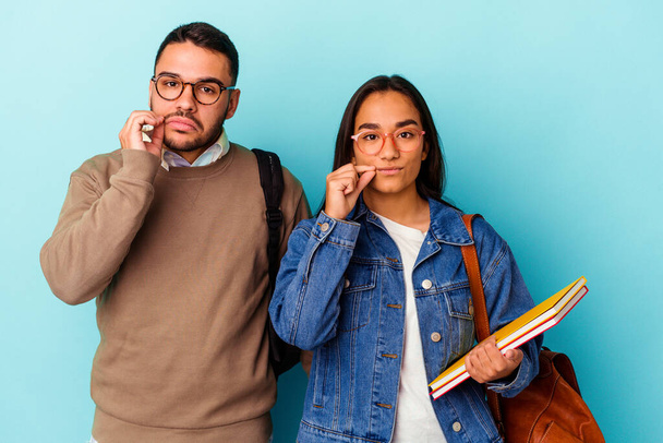 Junge gemischte Rasse Studentenpaar isoliert auf blauem Hintergrund mit Fingern auf den Lippen halten ein Geheimnis. - Foto, Bild
