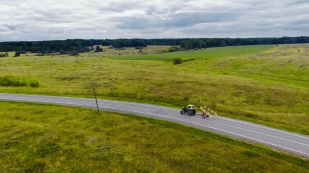 Egy mezőgazdasági gépekkel felszerelt traktor halad az úton. - Felvétel, videó