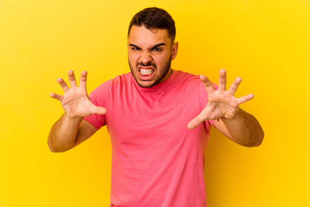 Young caucasian man isolated on yellow background showing claws imitating a cat, aggressive gesture. - Photo, Image