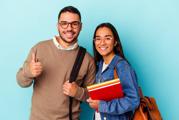 Young mixed race student couple isolated on blue background smiling and raising thumb up - Photo, Image