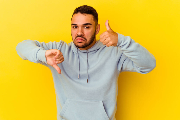 Young caucasian man isolated on yellow background showing thumbs up and thumbs down, difficult choose concept - Foto, Imagem