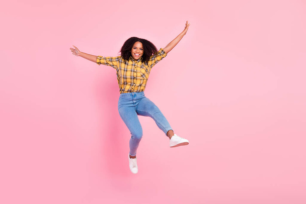 Photo of cheerful positive energetic lady jump raise hands wear plaid shirt jeans shoes isolated pink color background - Foto, Bild