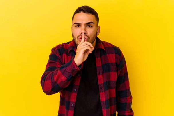 Young caucasian man isolated on yellow background keeping a secret or asking for silence. - Foto, Bild