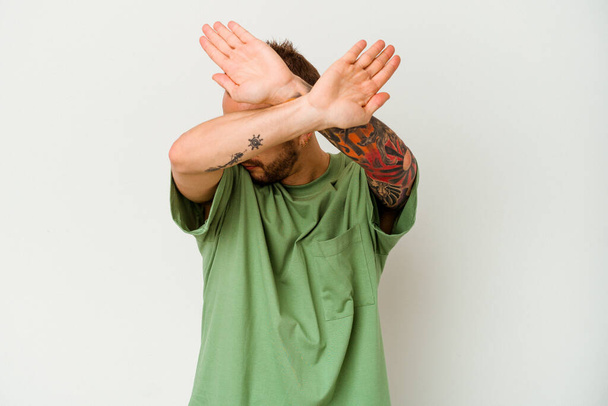 Young tattooed caucasian man isolated on white background keeping two arms crossed, denial concept. - Фото, зображення