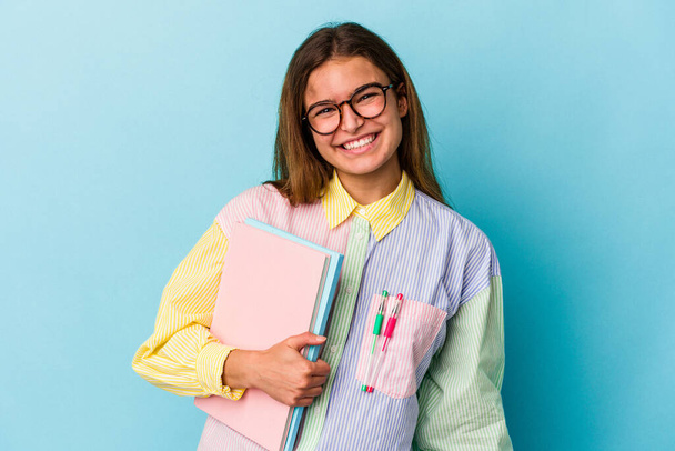 Jovem estudante caucasiano segurando livros isolados em fundo azul feliz, sorridente e alegre. - Foto, Imagem