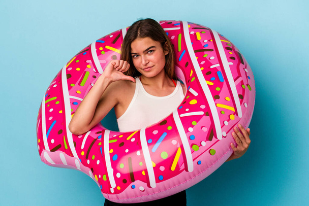Young caucasian woman with inflatable donut isolated on blue background showing a dislike gesture, thumbs down. Disagreement concept. - Photo, Image