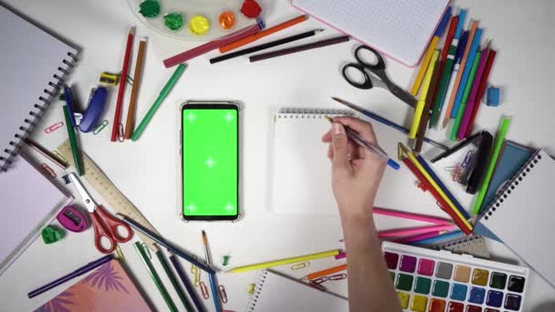 Вид зверху на стіл, повний шкільного приладдя та ручної стрічки людини на мобільному телефоні з зеленим екраном
 - Кадри, відео