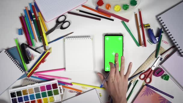 Mężczyzna stuka w smartfona z zielonym ekranem i zaczyna pisać w notebooku siedzi przy stole - Materiał filmowy, wideo