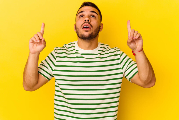 Young caucasian man isolated on yellow background pointing upside with opened mouth. - Foto, Imagen