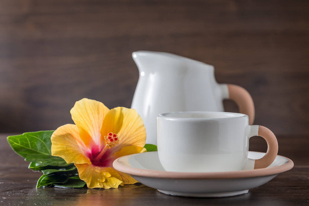 naturaleza muerta con una taza y una jarra de leche, colocadas junto a una flor de hibisco - Foto, Imagen