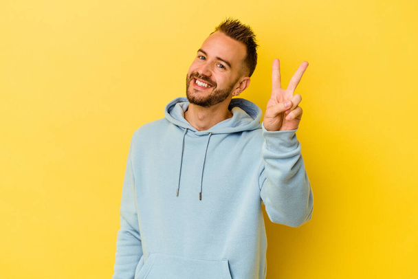 Young tattooed caucasian man isolated on yellow background joyful and carefree showing a peace symbol with fingers. - Photo, Image