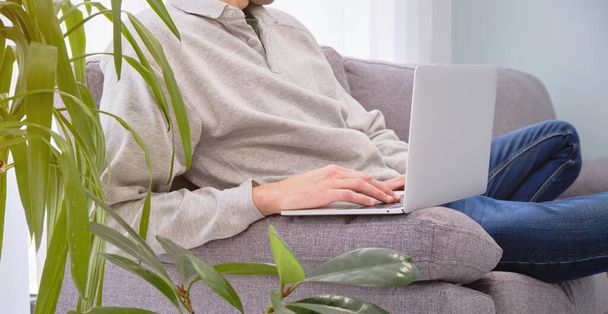 Male hands working at a laptop while sitting on the couch in yoga position working at home. - 写真・画像