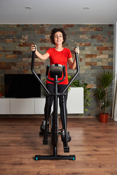 Woman training at home using elliptical cross trainer - Фото, изображение