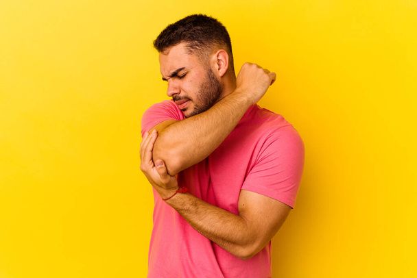 Young caucasian man isolated on yellow background massaging elbow, suffering after a bad movement. - Φωτογραφία, εικόνα
