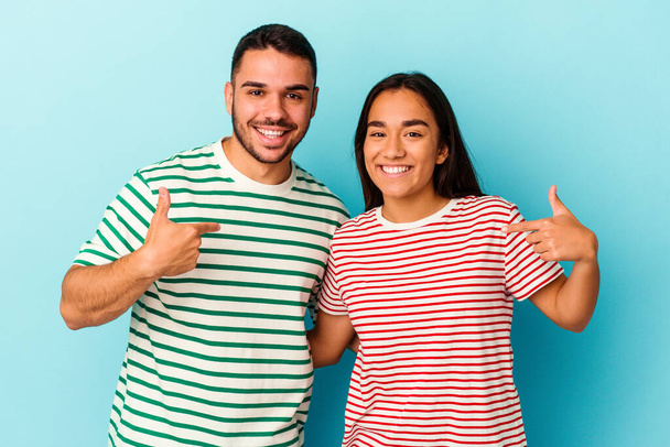 Jeune couple mixte isolé sur fond bleu personne pointant à la main vers un espace de copie chemise, fier et confiant - Photo, image
