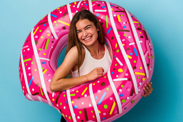Young caucasian woman with inflatable donut isolated on blue background laughing and having fun. - Fotoğraf, Görsel