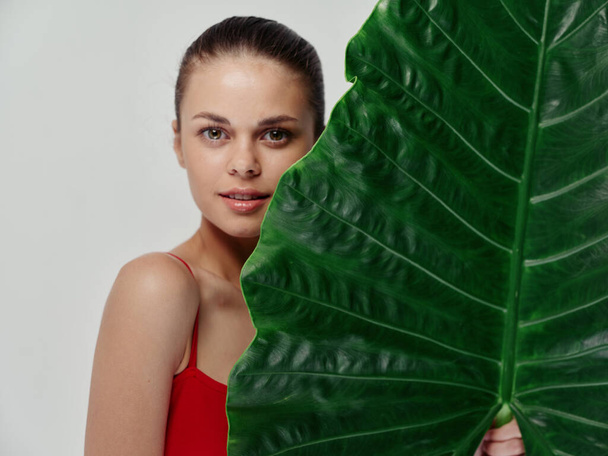 una mujer en traje de baño rojo se encuentra cerca de una hoja verde de una palmera modelo hombros desnudos - Foto, Imagen