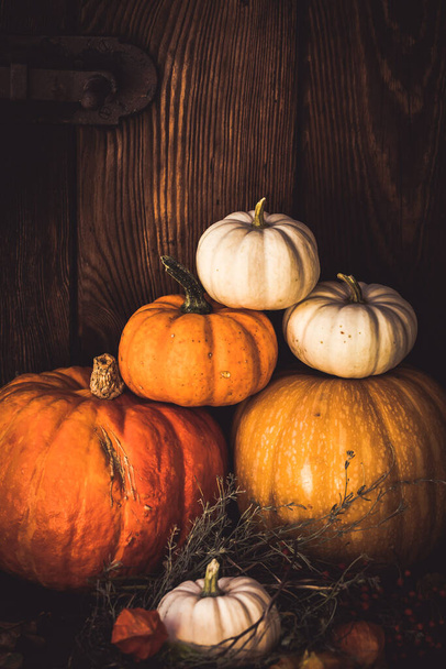 Stacked pumpkins of different sizes and colors with autumn decorations in front of a wooden wall, vertical with copy space - Fotoğraf, Görsel