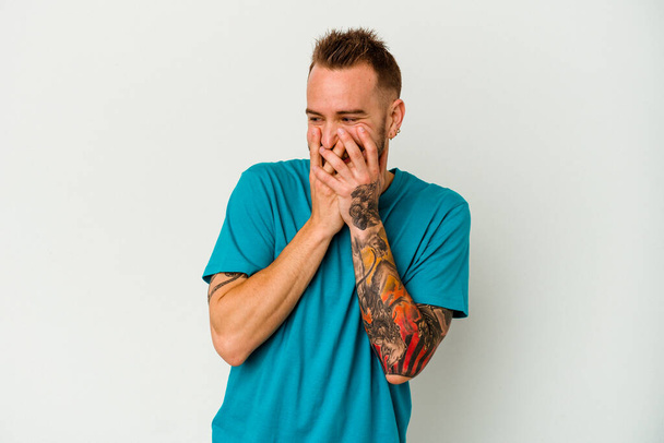 Λευκός άνδρας με τατουάζ, απομονωμένος σε λευκό φόντο γελώντας για κάτι, καλύπτοντας το στόμα με τα χέρια.. - Φωτογραφία, εικόνα