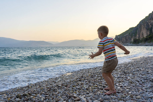 Deniz kenarındaki küçük çocuk suya taş atıyor.. - Fotoğraf, Görsel