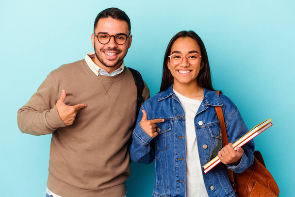 Junge gemischte Rasse Studentenpaar isoliert auf blauem Hintergrund Person zeigt mit der Hand auf ein Hemd Kopierraum, stolz und zuversichtlich - Foto, Bild