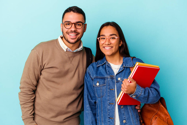 Young mixed race student couple isolated on blue background happy, smiling and cheerful. - Foto, Imagem