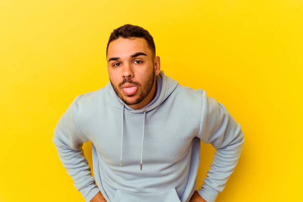 Young caucasian man isolated on yellow background funny and friendly sticking out tongue. - Zdjęcie, obraz
