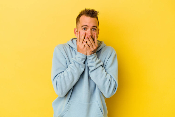Young tattooed caucasian man isolated on yellow background shocked, covering mouth with hands, anxious to discover something new. - Photo, Image