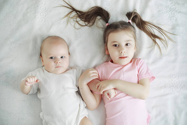 Kinderen liggen op het bed naast de pasgeboren baby, zusje. Emoties van kinderen. - Foto, afbeelding