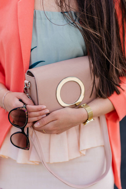 A vertical shot of a fashionable female outfit with a light pink bag and sunglasses - Фото, зображення