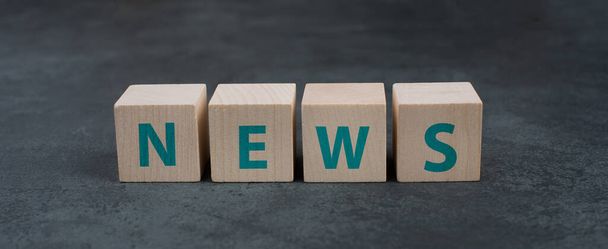The word news is standing on wooden blocks, dark background - Foto, Imagem