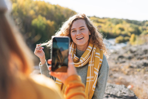 Młode piękne kobiety podróżujące przyjaciele robienie zdjęć na telefon komórkowy na tle gór i rzeki, turystyka na jesieni charakter - Zdjęcie, obraz
