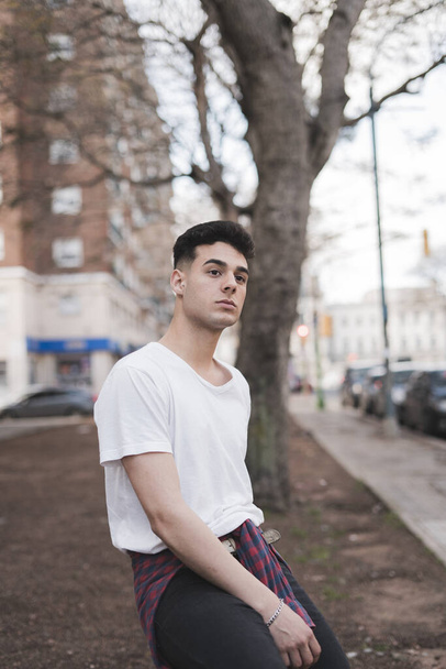 A vertical shot of a young stylish male in a white t-shirt posing on the street - Foto, imagen